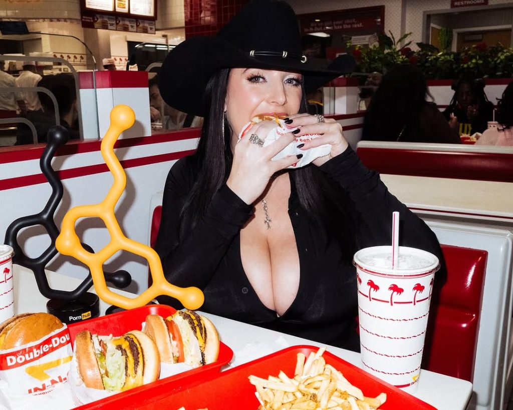 Big tit girl dressed in a country outfit taking a bite out of a burger at a restaurant