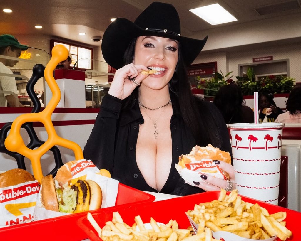 Cowgirl with big tits showing cleavage while eating a French fry at a burger restaurant