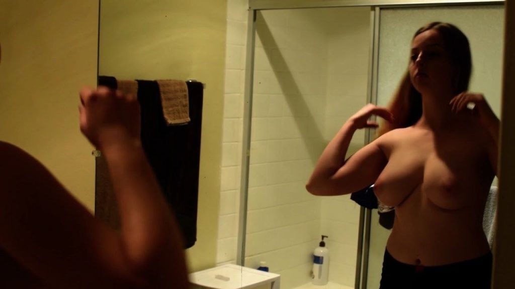 Topless girl with big boobs looks at herself in the mirror