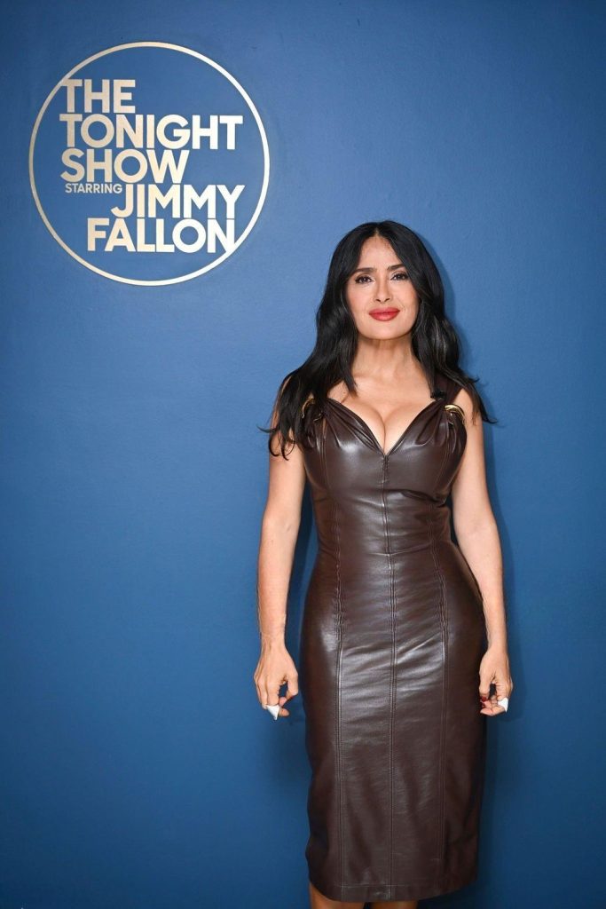 Salma Hayek showing cleavage in a tight dress against a blue background