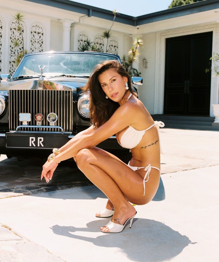 Side view of a sexy bikini babe squatting down in front of a luxurious car
