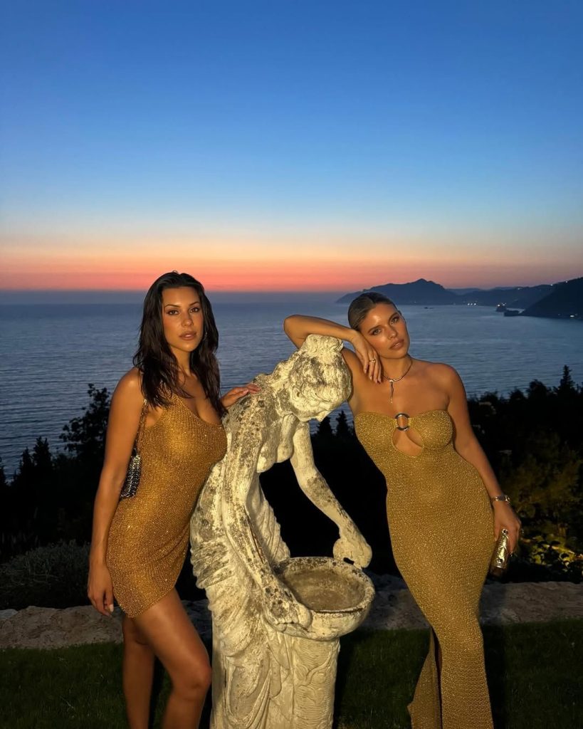 Two sexy women posing in the same tight golden dress with a nice sunset in the background