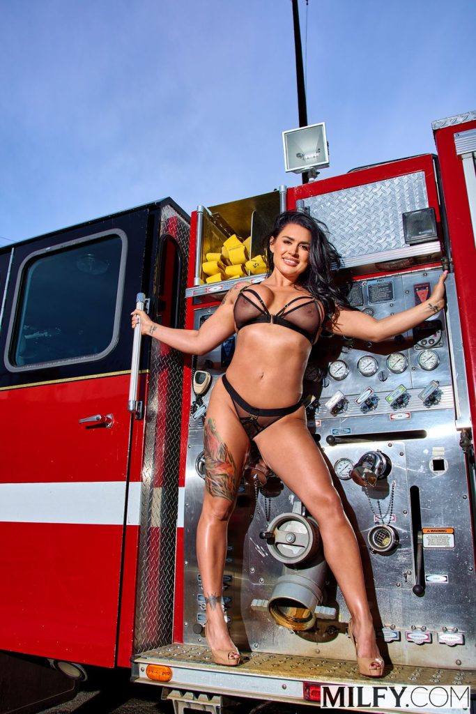 Busty woman posing in sexy lingerie on top of a fire truck