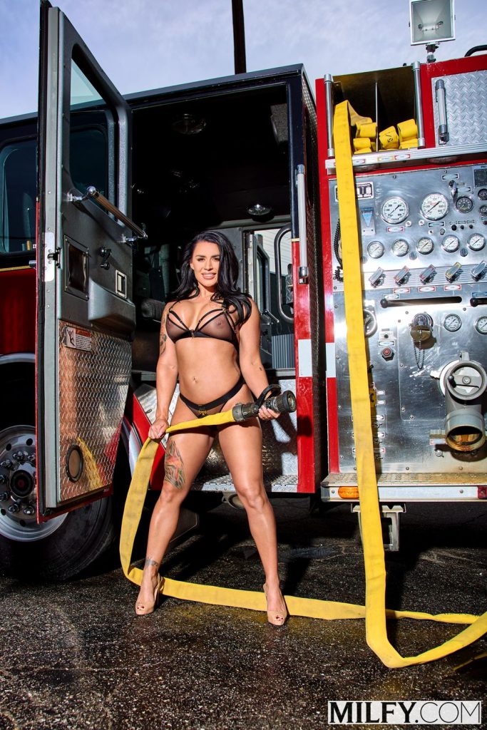 Smoking hot lingerie babe posing with a hose in front of a fire truck
