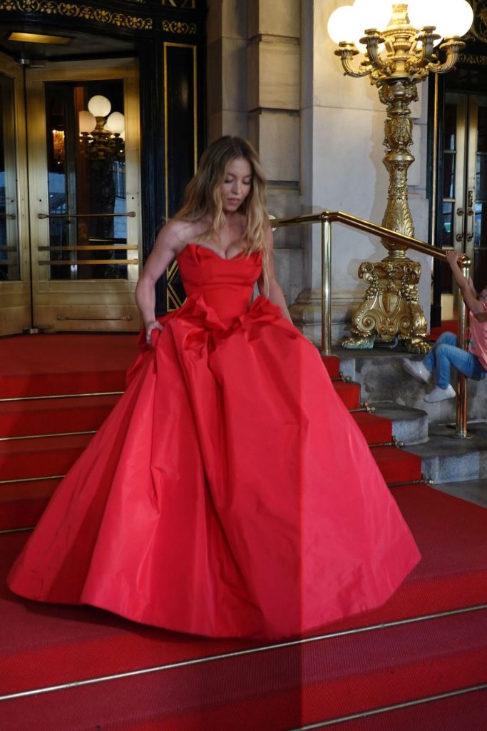 Sydney Sweeney walking down red carpet draped stairs in a red dress