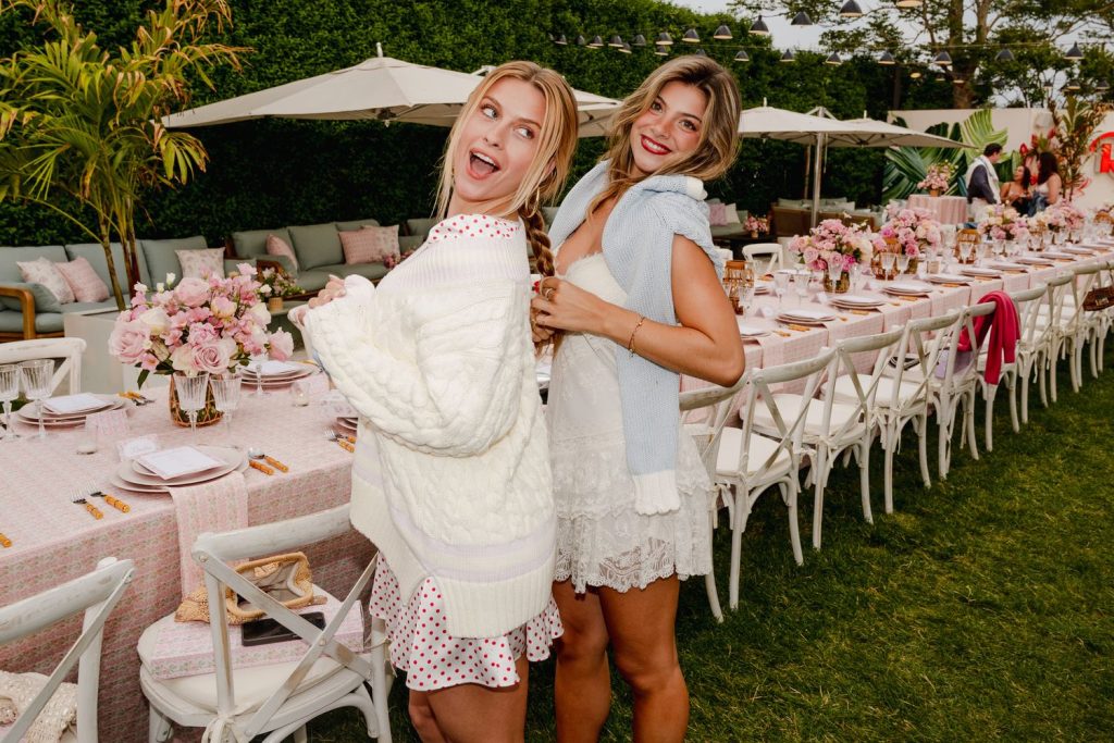 A couple of hot swimsuit models look over their shoulders while standing next to a table at a picnic event