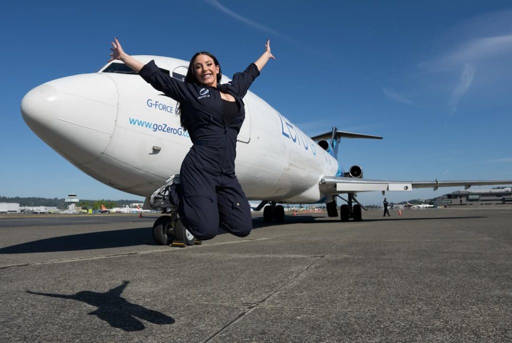 Angela White jumping up in the air in front of a big air plane