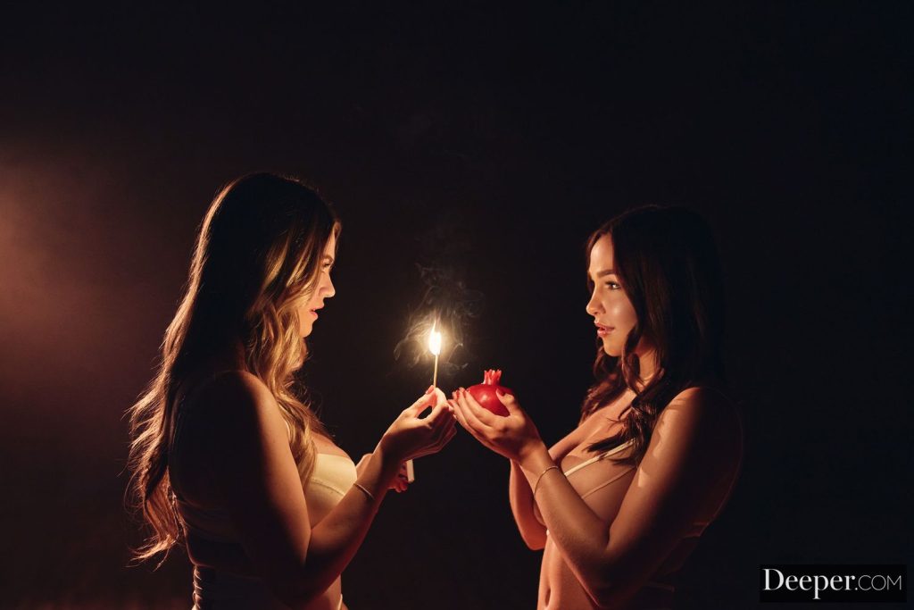 Two pretty babes light a match in the dark while looking at each other