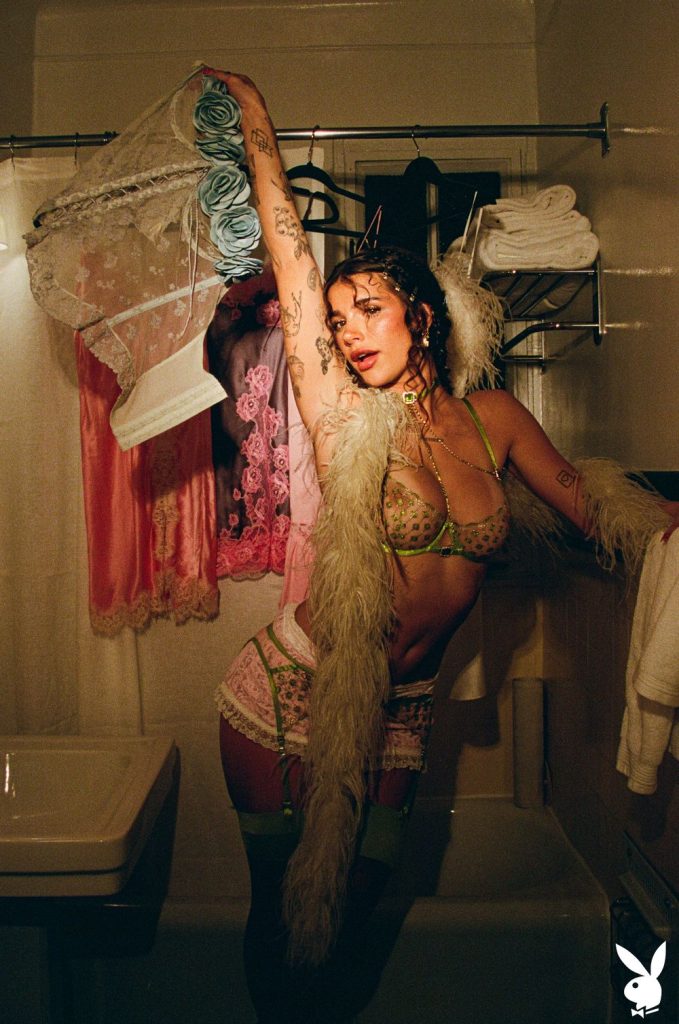 Busty brunette showing boobs in a sheer bra while raising one hand in the air. She's in sexy lingerie and feather boa around her neck