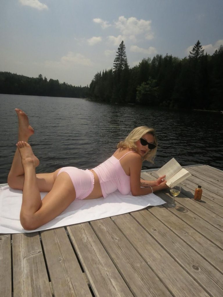 Sexy blonde on her stomach on a lakeside dock and reading a book
