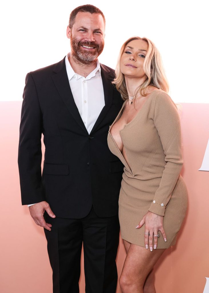Blonde babe showing off her big boobs in a tight dress next to a man on the red carpet