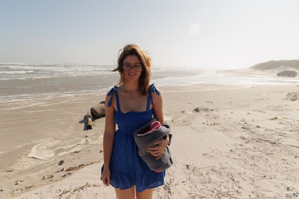 Pretty girl in a blue dress and glasses posing on the beach on a windy day