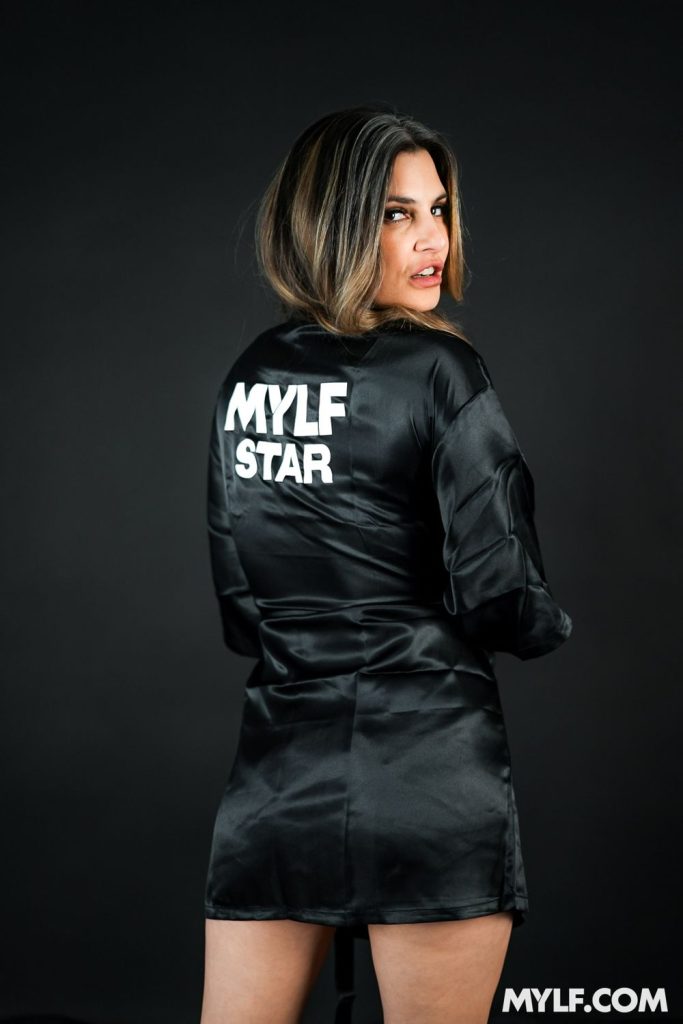 Sexy MILF in a black robe with her back turned to show us that it says MYLF STAR on the back of it