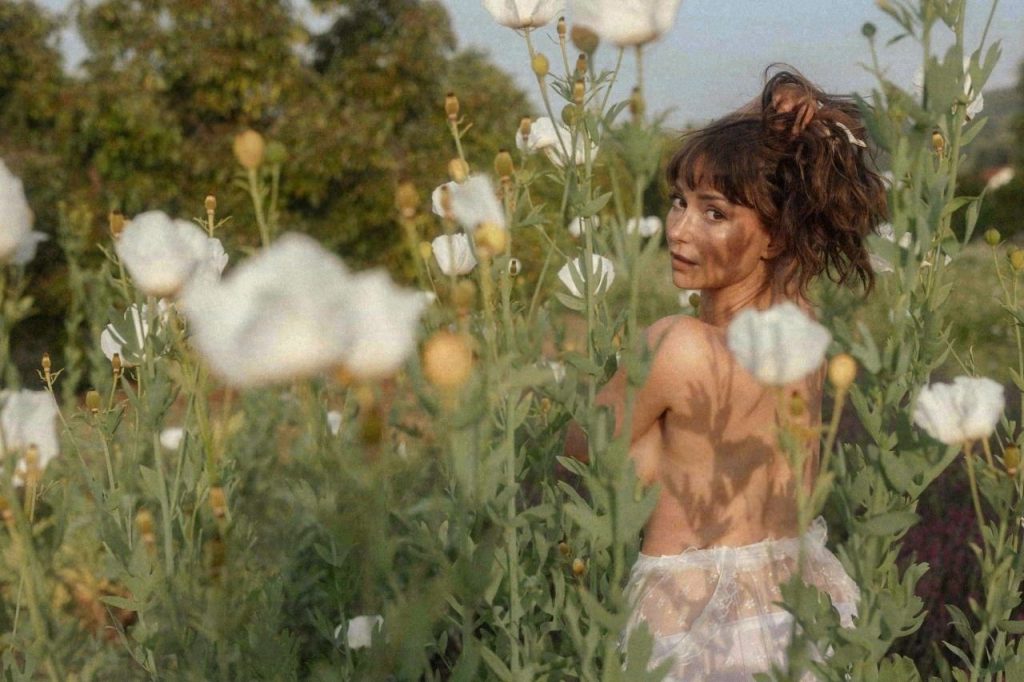 Milana Vayntrub topless and showing off her bare back in a meadow