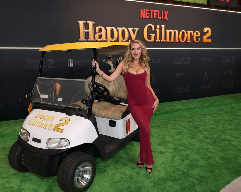 Wide view of a sexy blonde in a red dress posing next to a Golf cart at a movie premiere