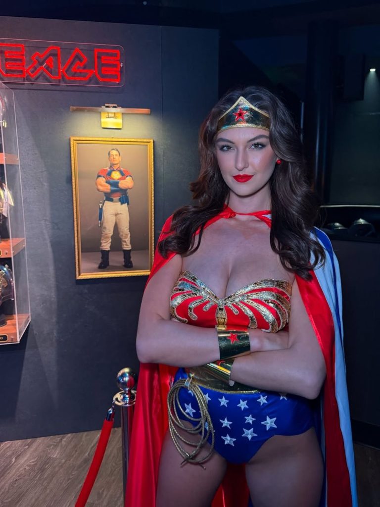 Busty babe cosplay as Wonder Woman posing in front of action figure at Comic Con