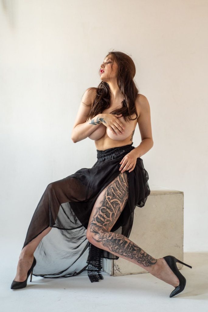 Topless woman with big boobs in a black skirt and sitting on a cube