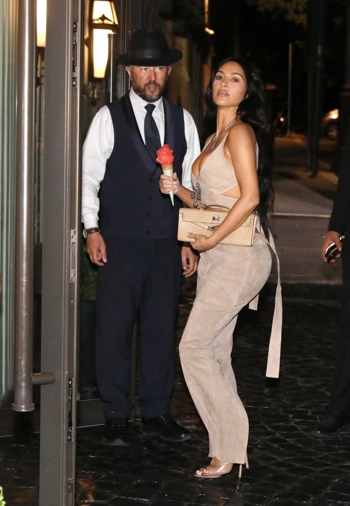 Kim Kardashian curvy from the side while holding an ice cream cone in front of hotel staff