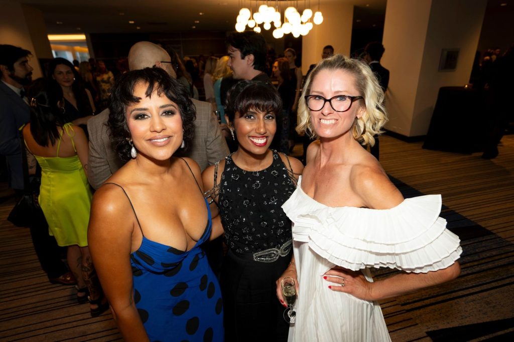 Down blouse view of Agam Darshi posing with two other women at an event