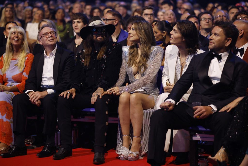 Elizabeth Hurley sitting down in the front row of an audience wearing a silver dress