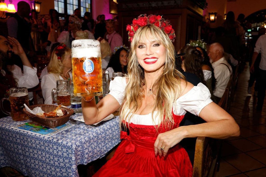 Heidi Klum sitting down and holding up a big glass of beer