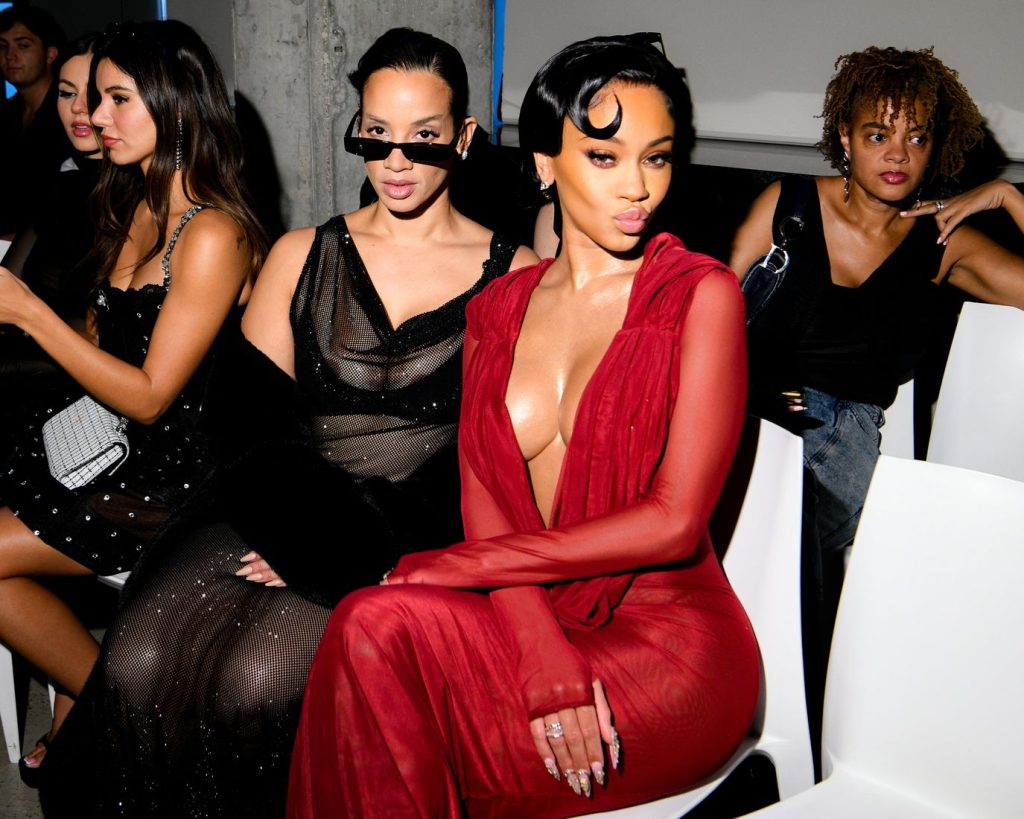 Saweetie sitting next to a woman wearing a black dress