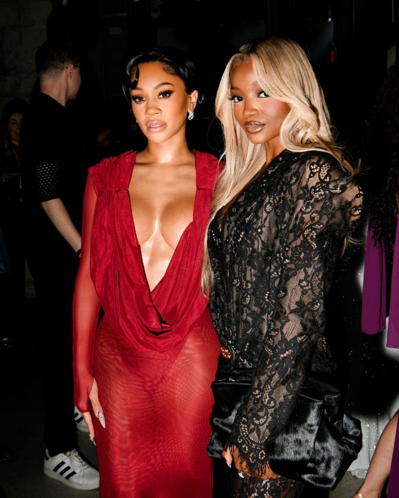 Saweetie posing next to a woman wearing a sexy black lace dress