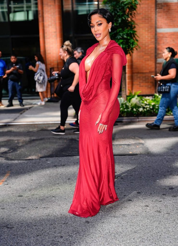 Saweetie posing to the side in a red dress