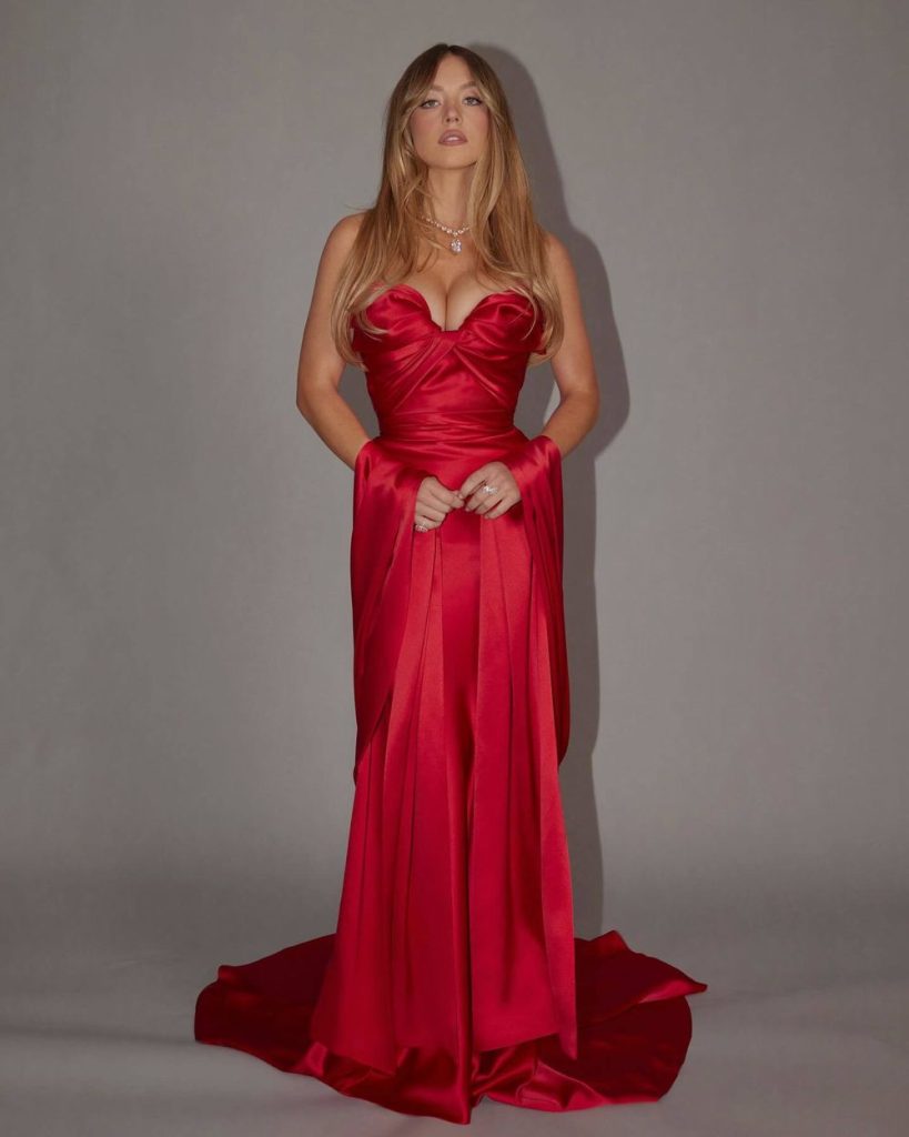 Sydney Sweeney posing in the red dress for a photo shoot against a grey background