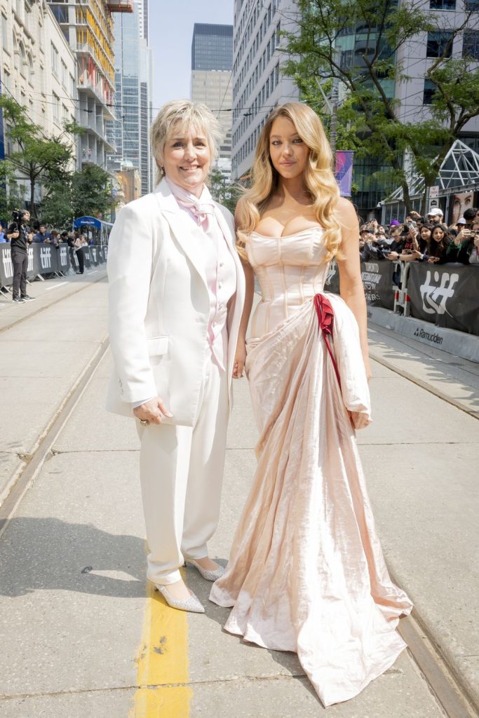 Sydney Sweeney and Christy Martin posing together on an empty street lines with crowds of people in Toronto