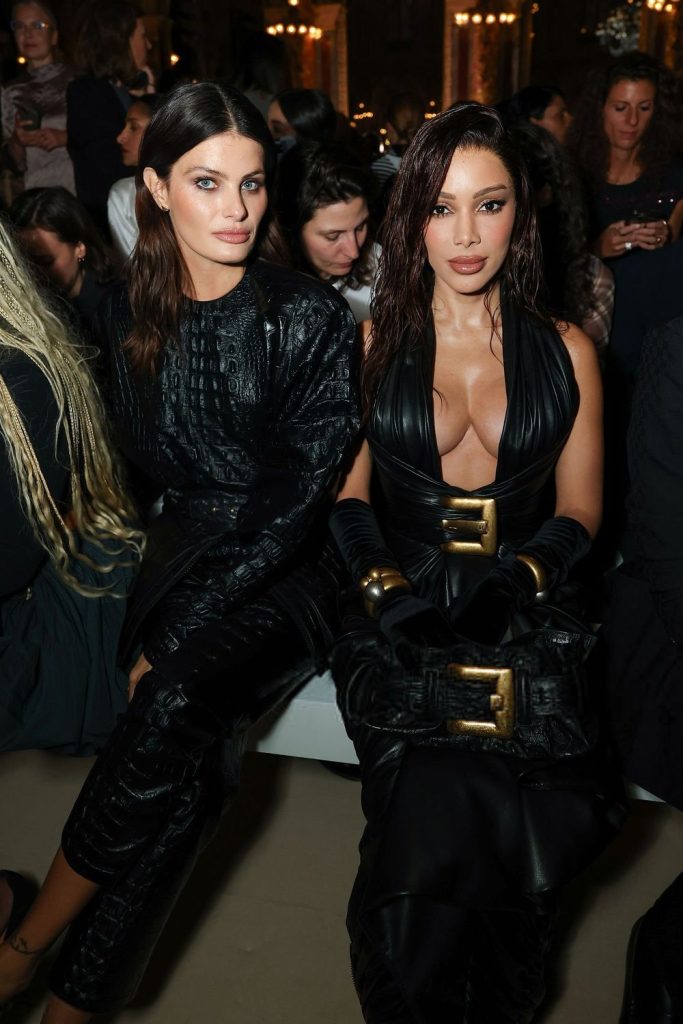 Anitta sits next to another lady at a fashion show