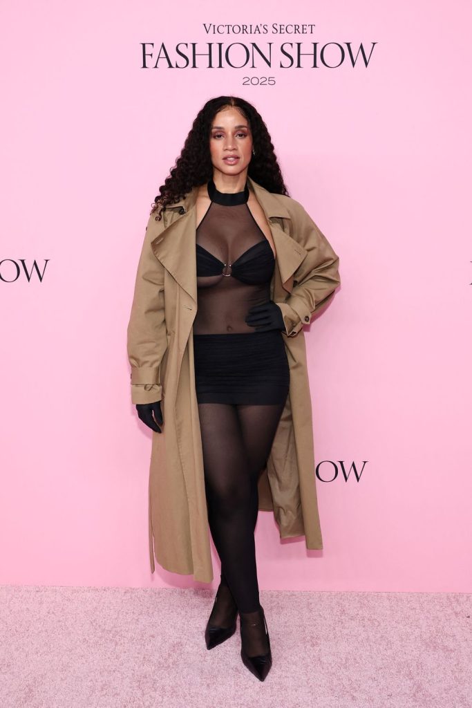 Dascha Polanco posing in a black and semi-sheer outfit against a pink background