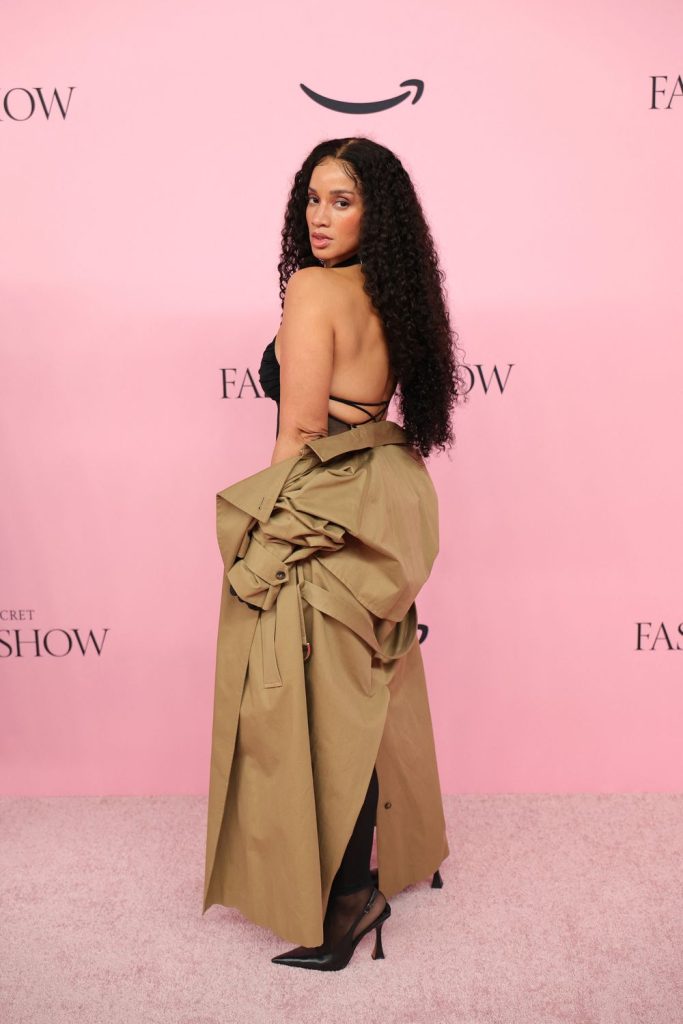 Dascha Polanco turned to the side and letting a coat hang off her hips to reveal her back