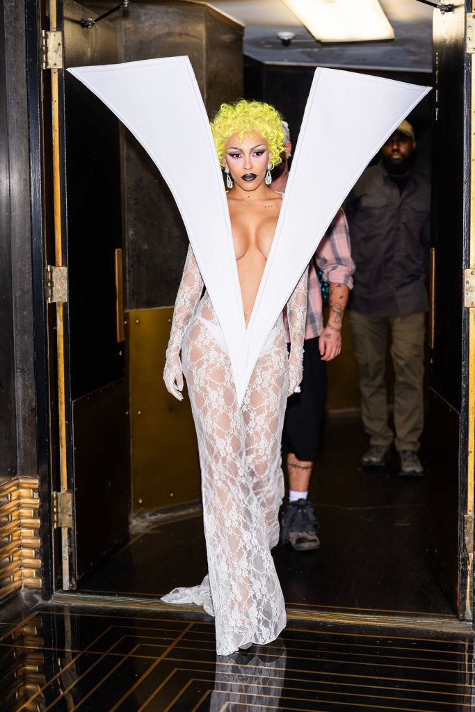 Doja Cat steps inside wearing a semi-sheer white dress that is shaped like a big V