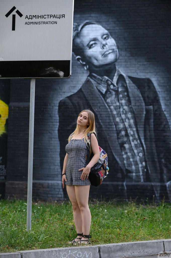 Blonde posing in front of big street art of a man in a suit