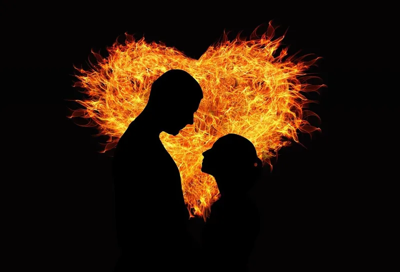 Silhouette of a couple looking at each other with a fiery heart in the background