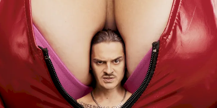 Close up of a tiny man's head sitting between a pair of gigantic breasts