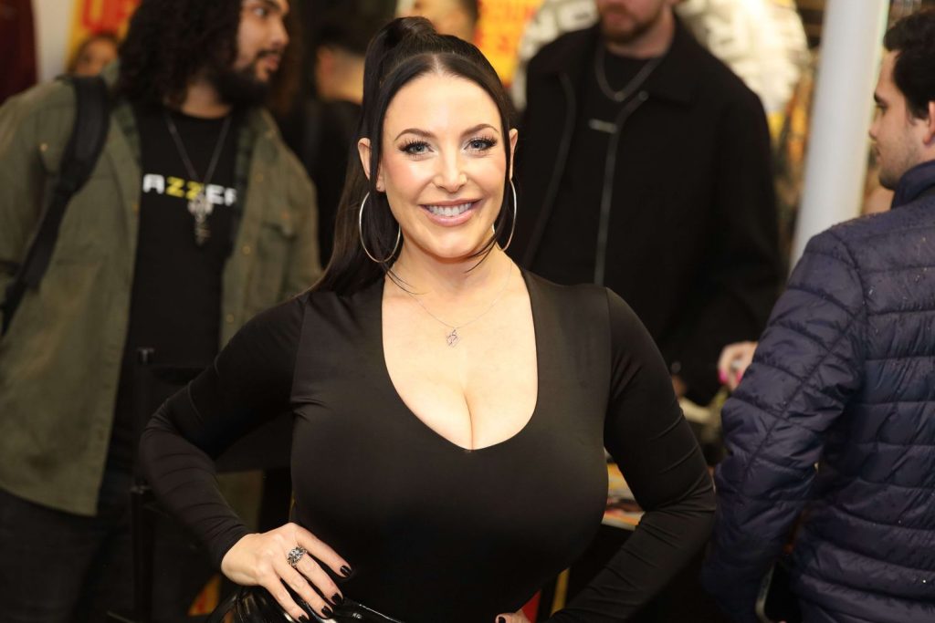 Wide angle view of porn star Angela White posing with two hands on her hips and with people in the background