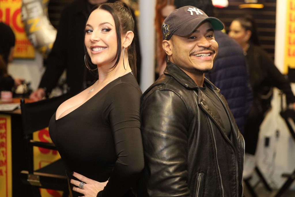 Wide angle view of Angela White posing back to back with a fan