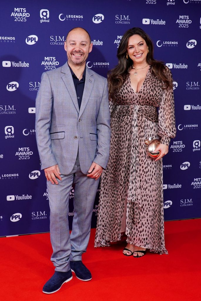 Full body front view of Kelly Brook posing next to a man on the red carpet