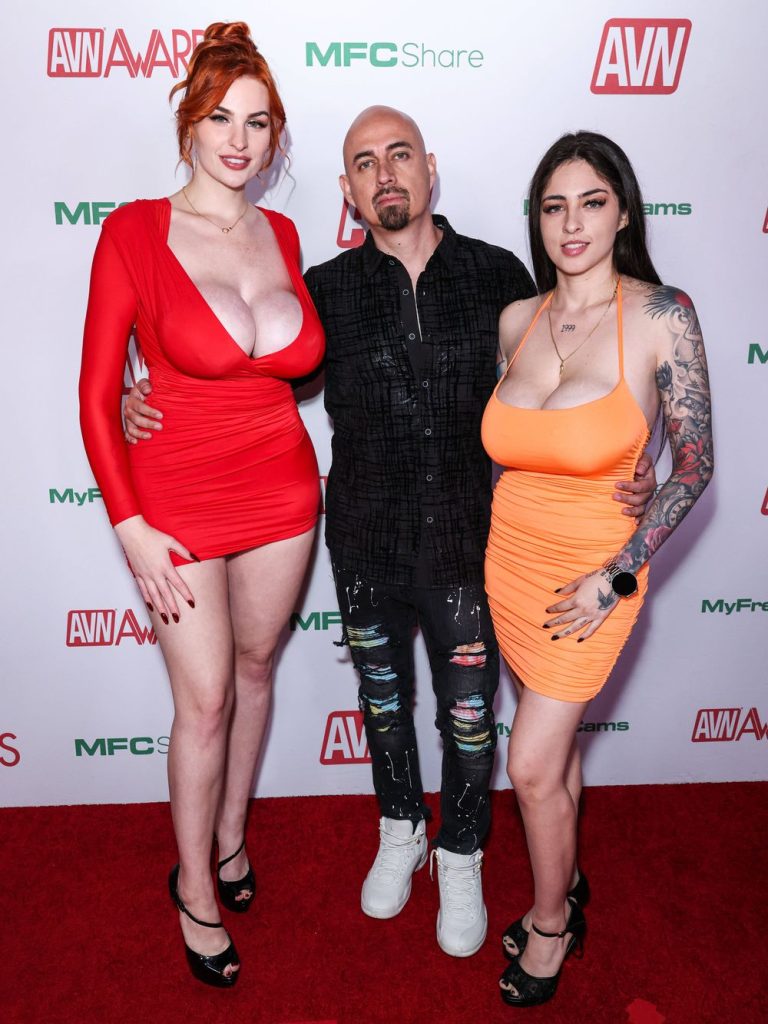 Full body front view of two female porn stars in tight dresses posing with a man between them