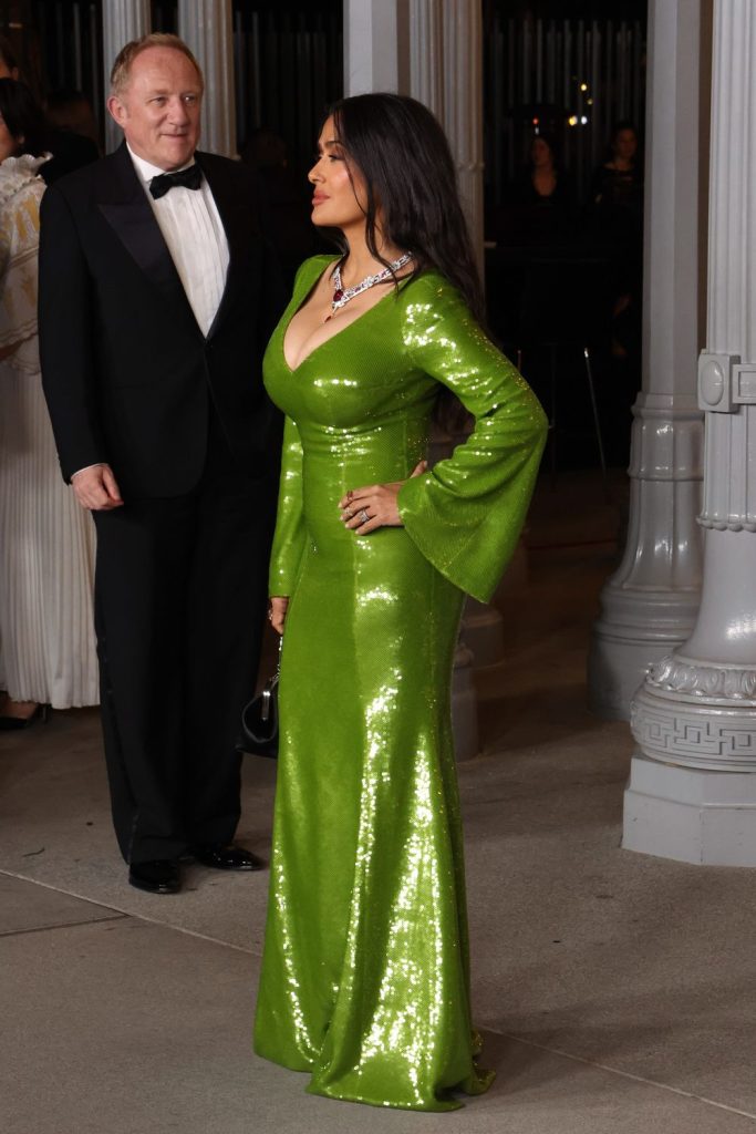Side view of Salma Hayek posing with her husband in the background