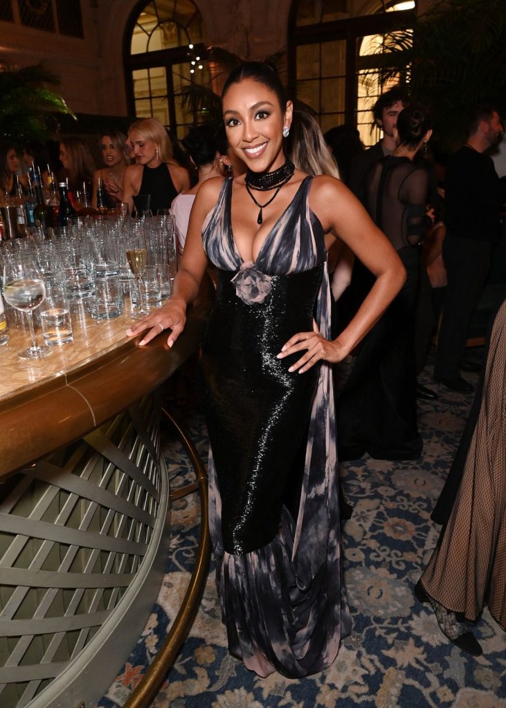 Front full body view of Tayshia Adams posing next to a bar at a party