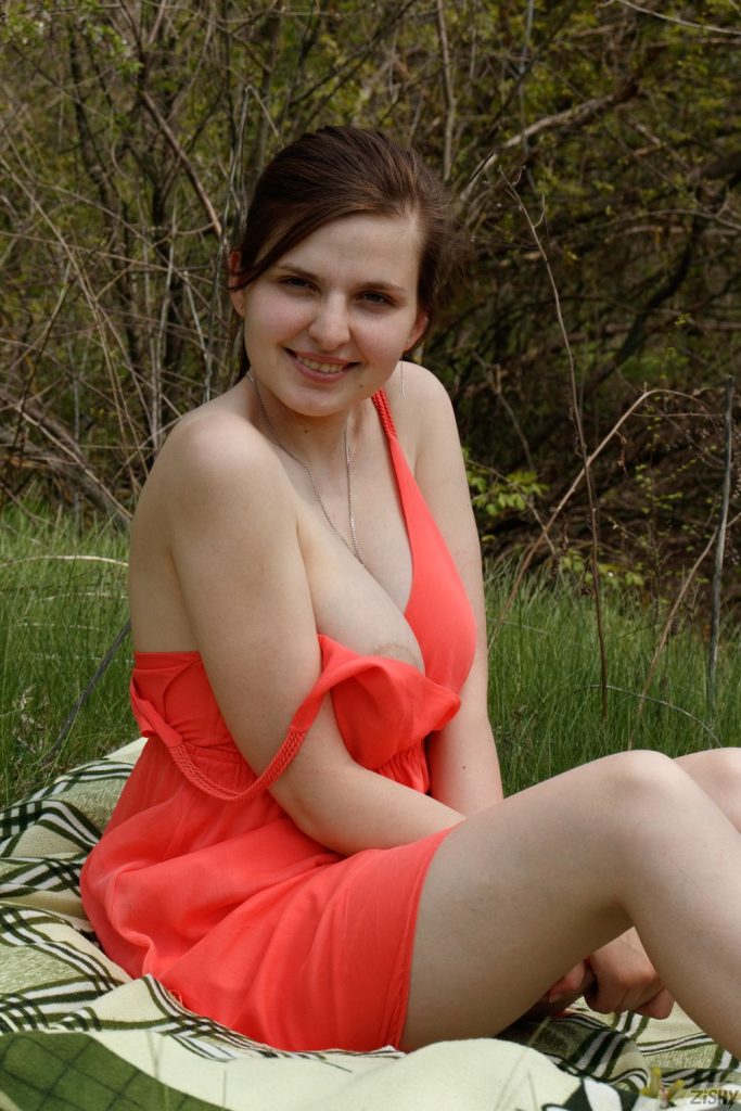 Frontal side view of woman sitting down in the grass with half her dress pulled down