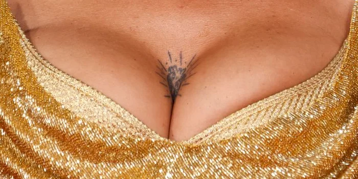 Close up of female breasts in a golden dress. There is a small tattoo at the top and middle of her chest