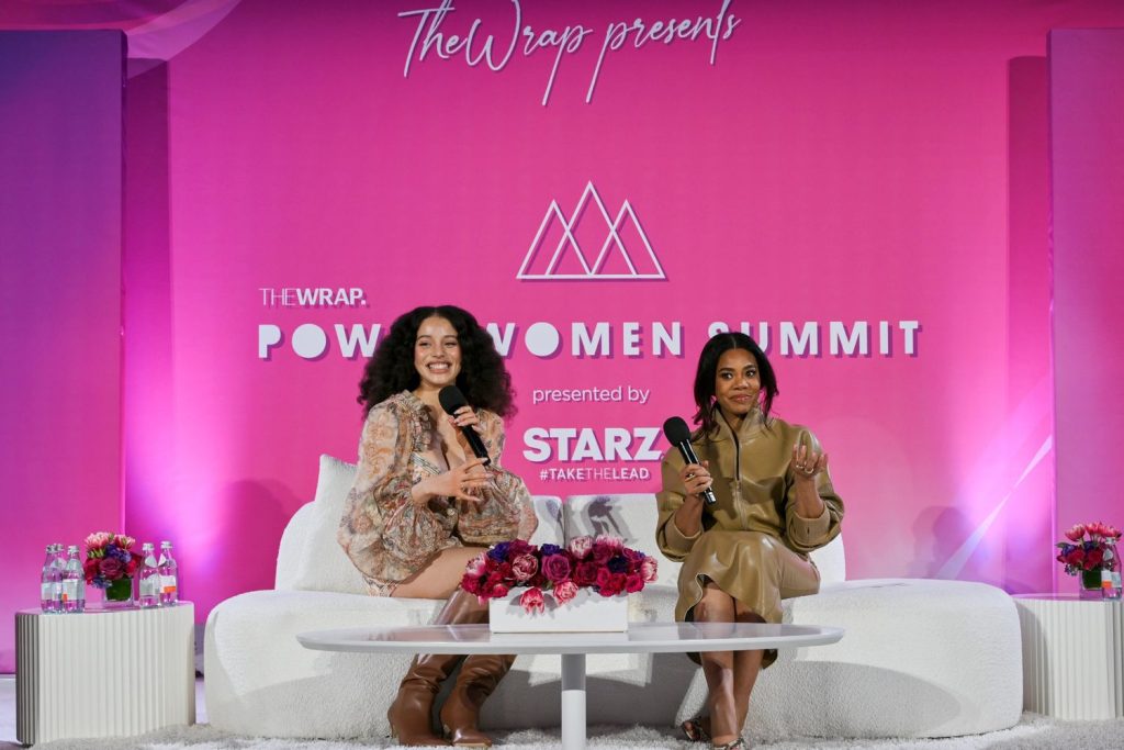 Far away view of two black actresses sitting next to each other in a sofa on a stage