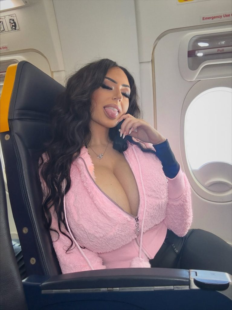 Woman with large breasts snaps a selfie while sitting in an airplane
