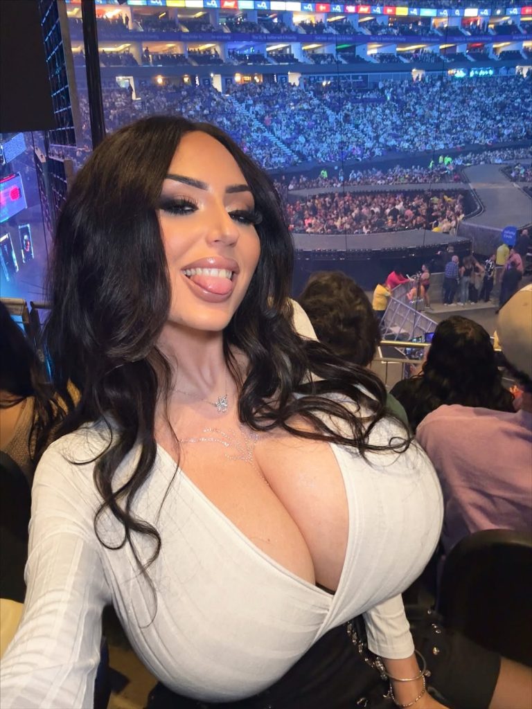 Woman with large breasts snaps a selfie from inside a sports stadium