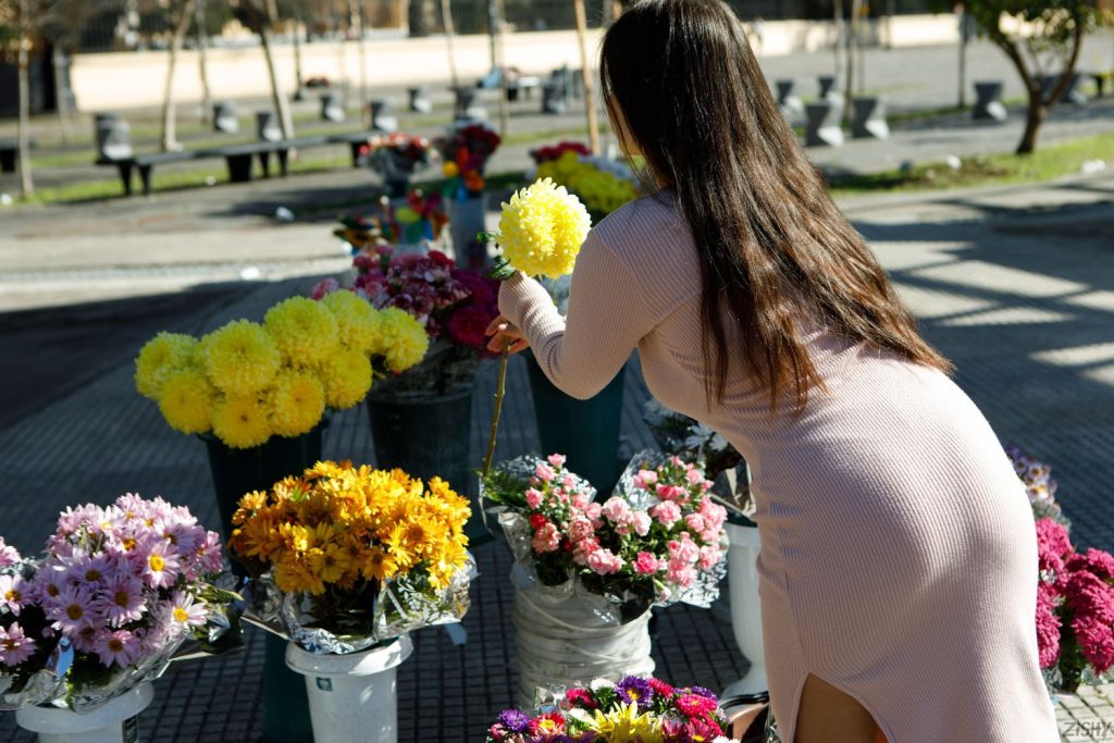 Backside view of curvy girl leaning forward to grab flowers from an on street flower stand
