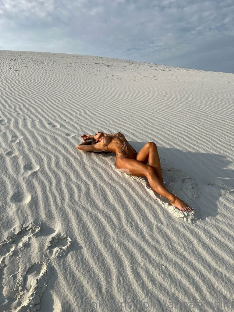 Far away view of nude woman laying on her back in a sand dune